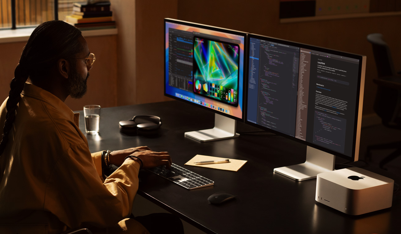 Seorang profesional yang bekerja menggunakan Mac Studio dan dua monitor Studio Display