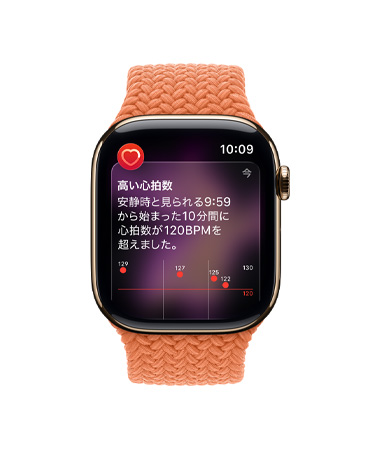 ゴールドチタニウムケースのApple Watch Series 11。高い心拍数の通知が表示され、ターメリックのブレイデッドソロループバンドが取りつけられている