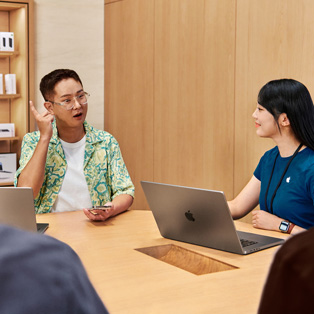 MacBook을 갖고 있는 Apple Store 직원이 다른 사람과 상호작용하는 모습.
