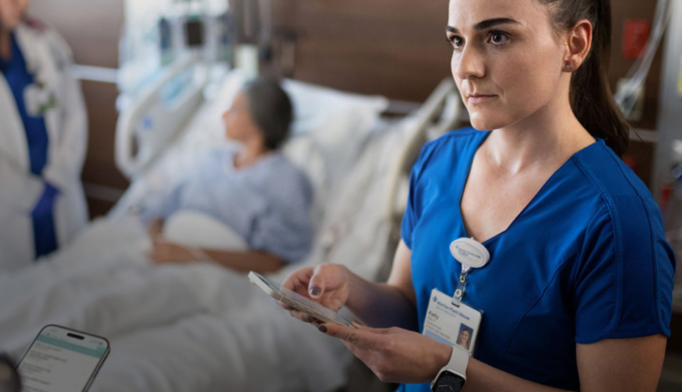 A nurse texting on her iPhone while another provider speaks to a patient.